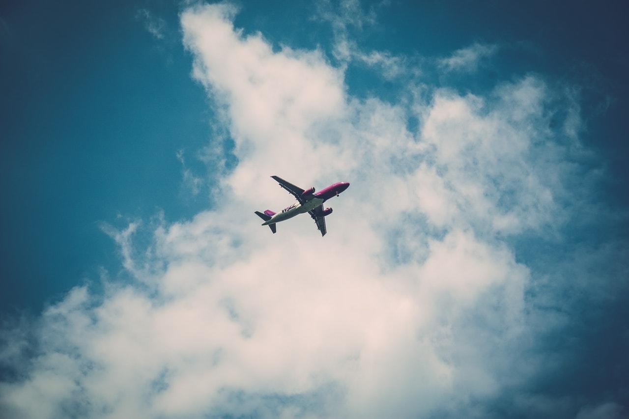 An airplane flying high against a backdrop of white clouds and a bright blue sky.