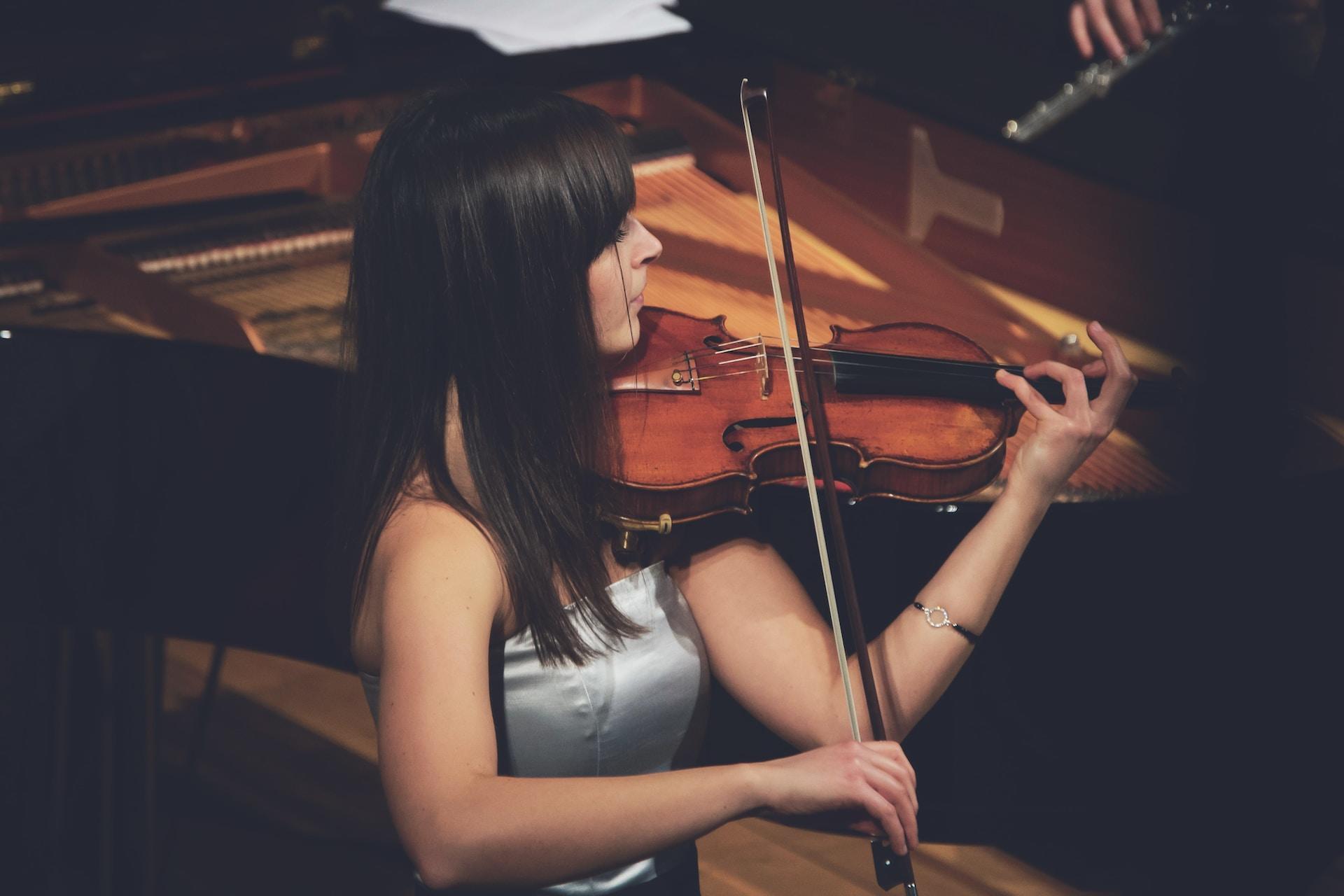 A woman playing violin in front of a piano.