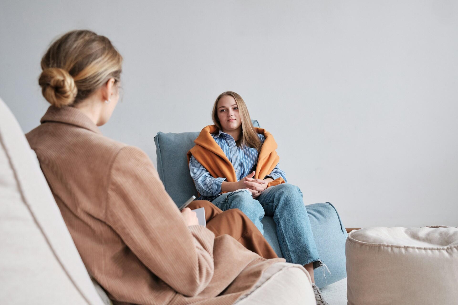 A woman in blue talks with a woman dressed in beige.