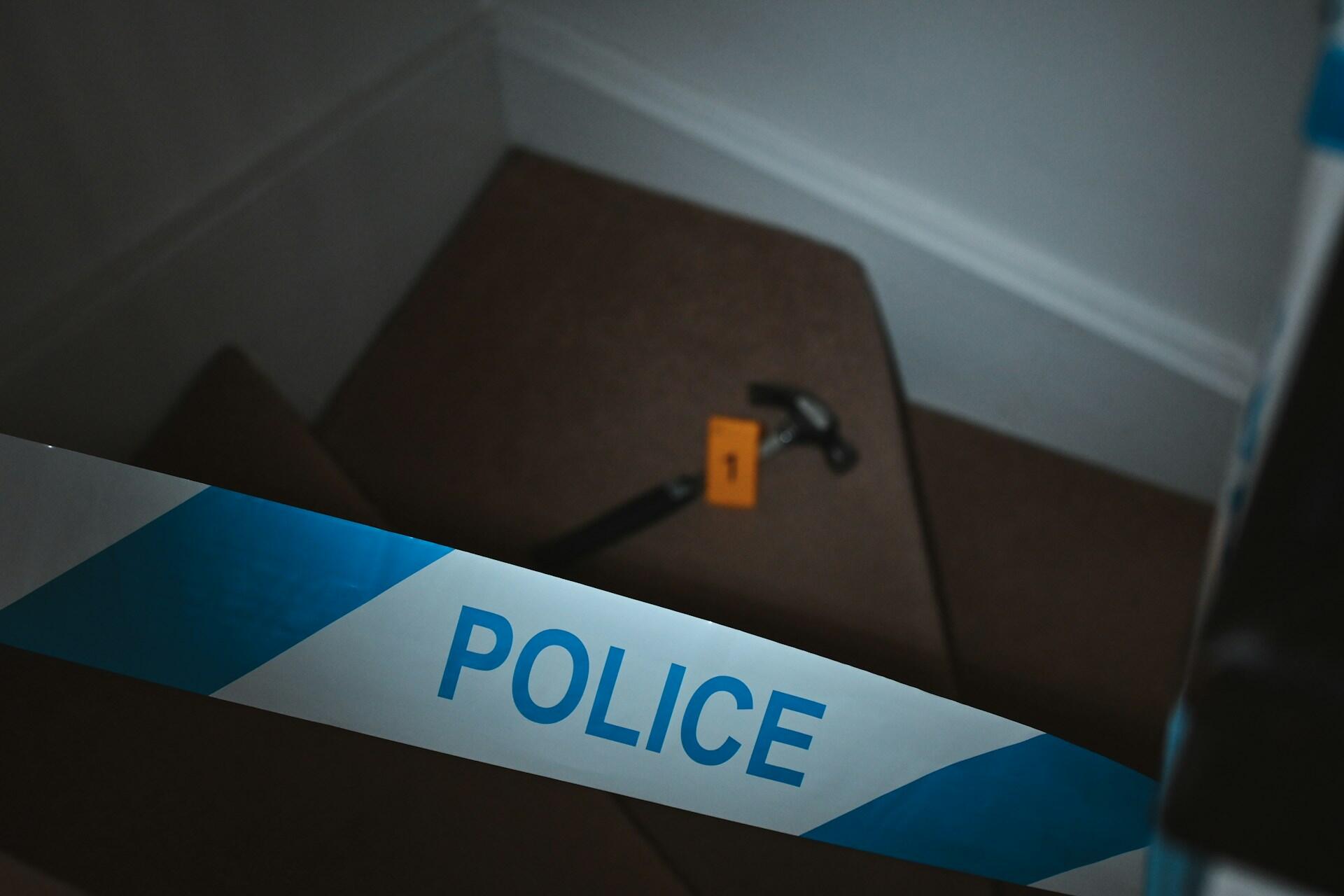A hammer laying on a staircase blocked with police tape.