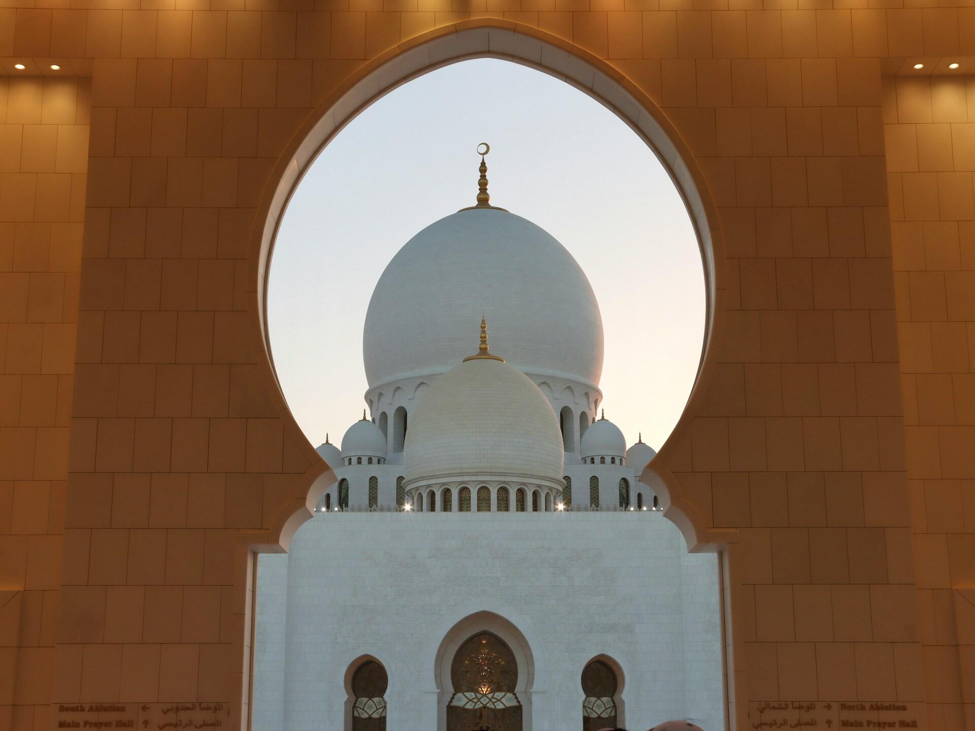 A view of the majestic Sheikh Zayed Grand Mosque dome framed by a large arch.