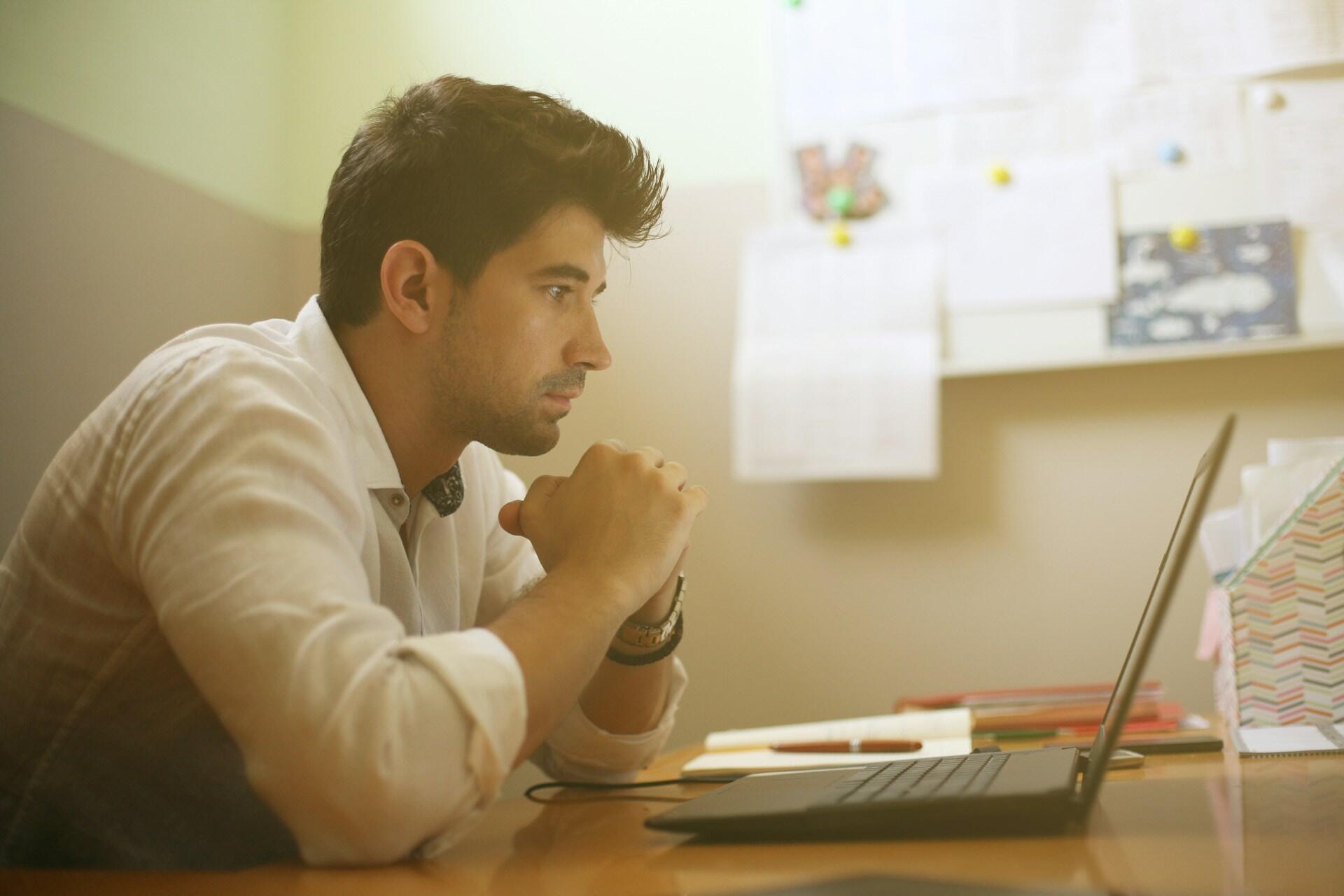 A person sits in front of an open computer with a bright light on nearby.