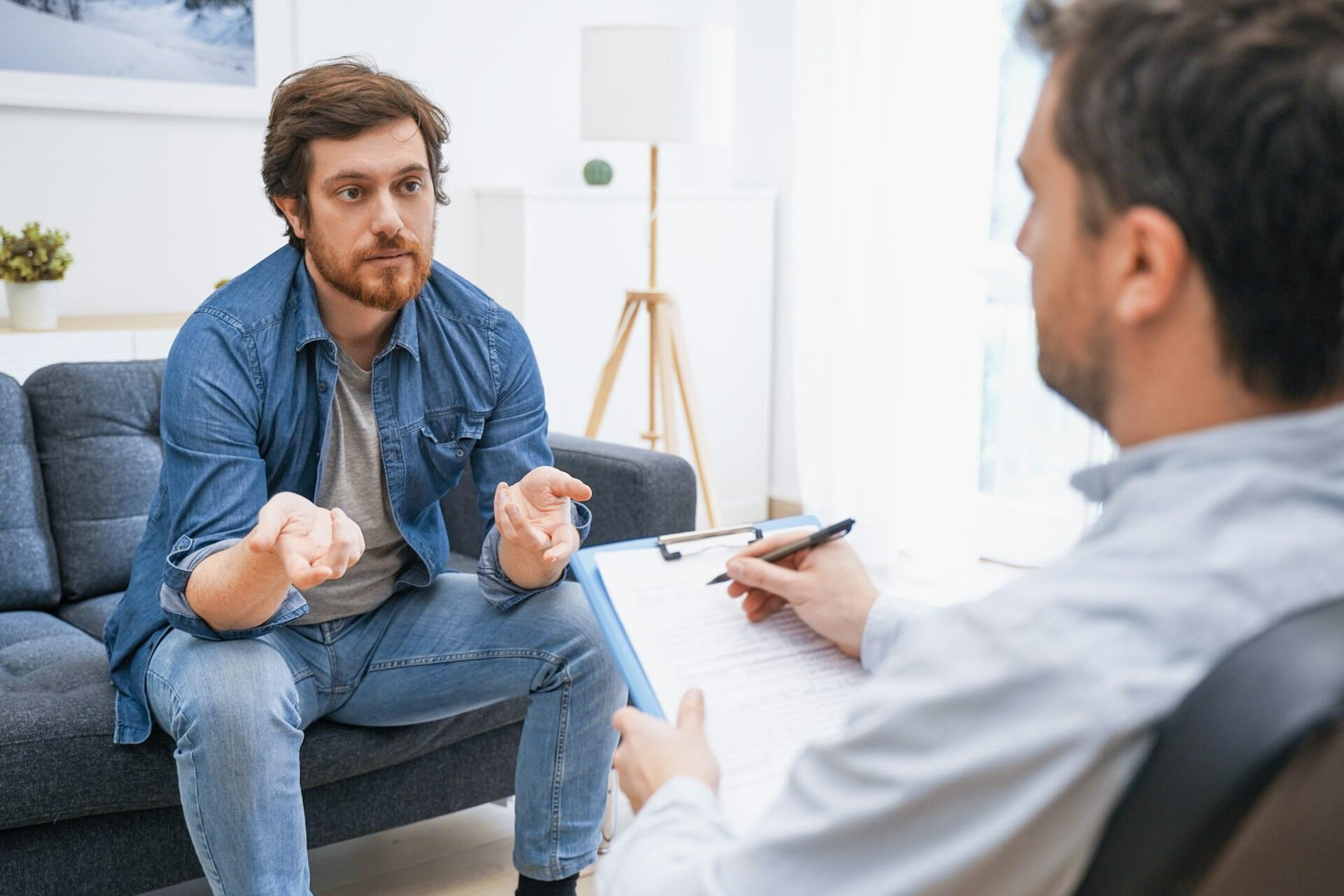 Two men wearing blue sit in an office, talking.