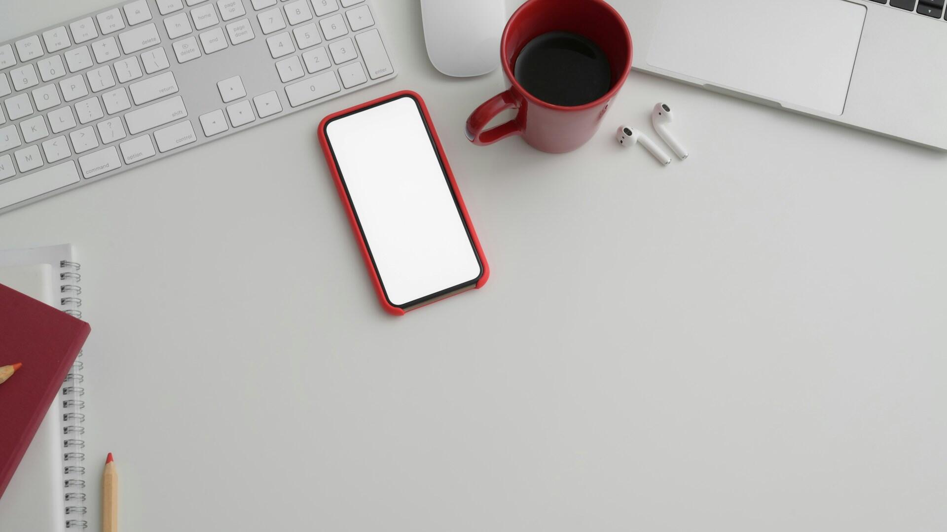 A red smartphone with a blank screen rests on a white desk.