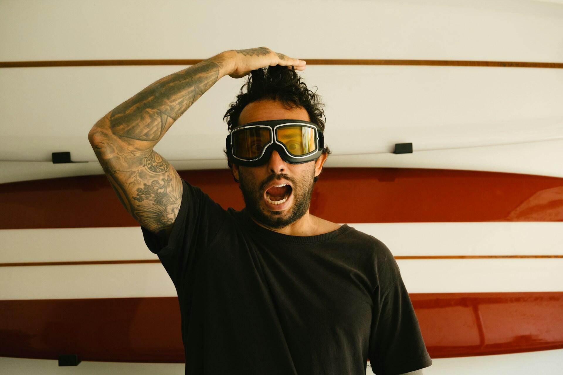 A man wearing yellow goggles in front of a surfboard.