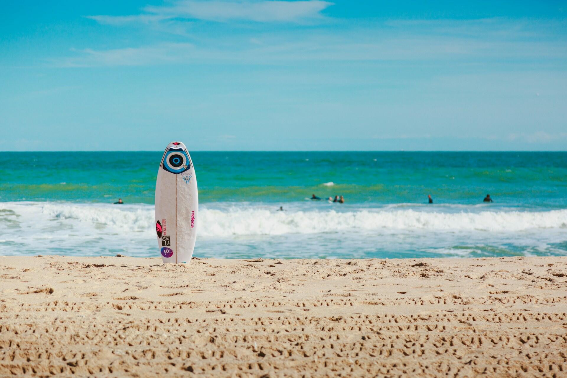 A surfboard planted on a beach with the sea behind it.
