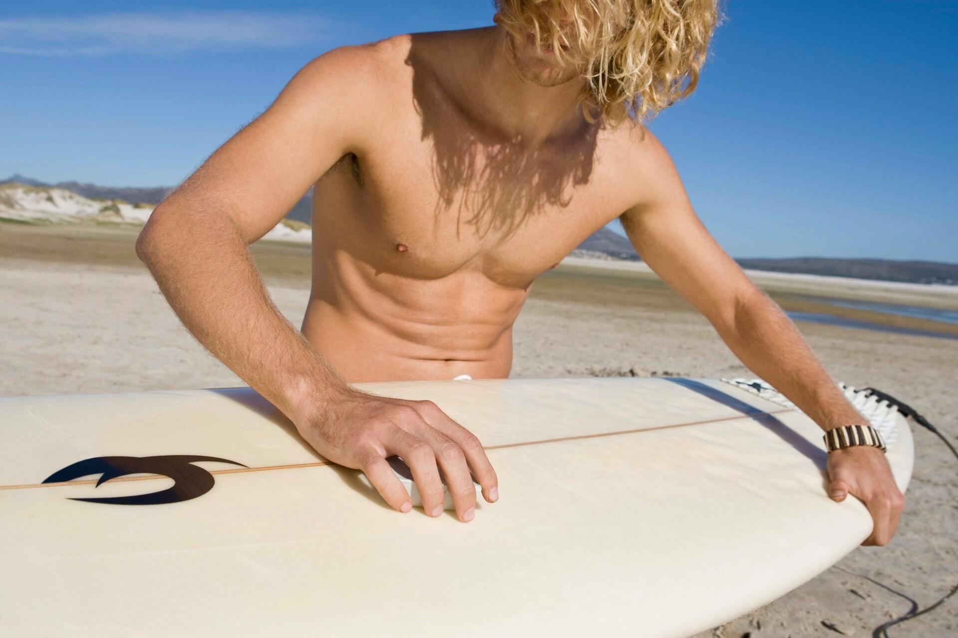 A person applying surf wax to a white surfboard on a sunny day.
