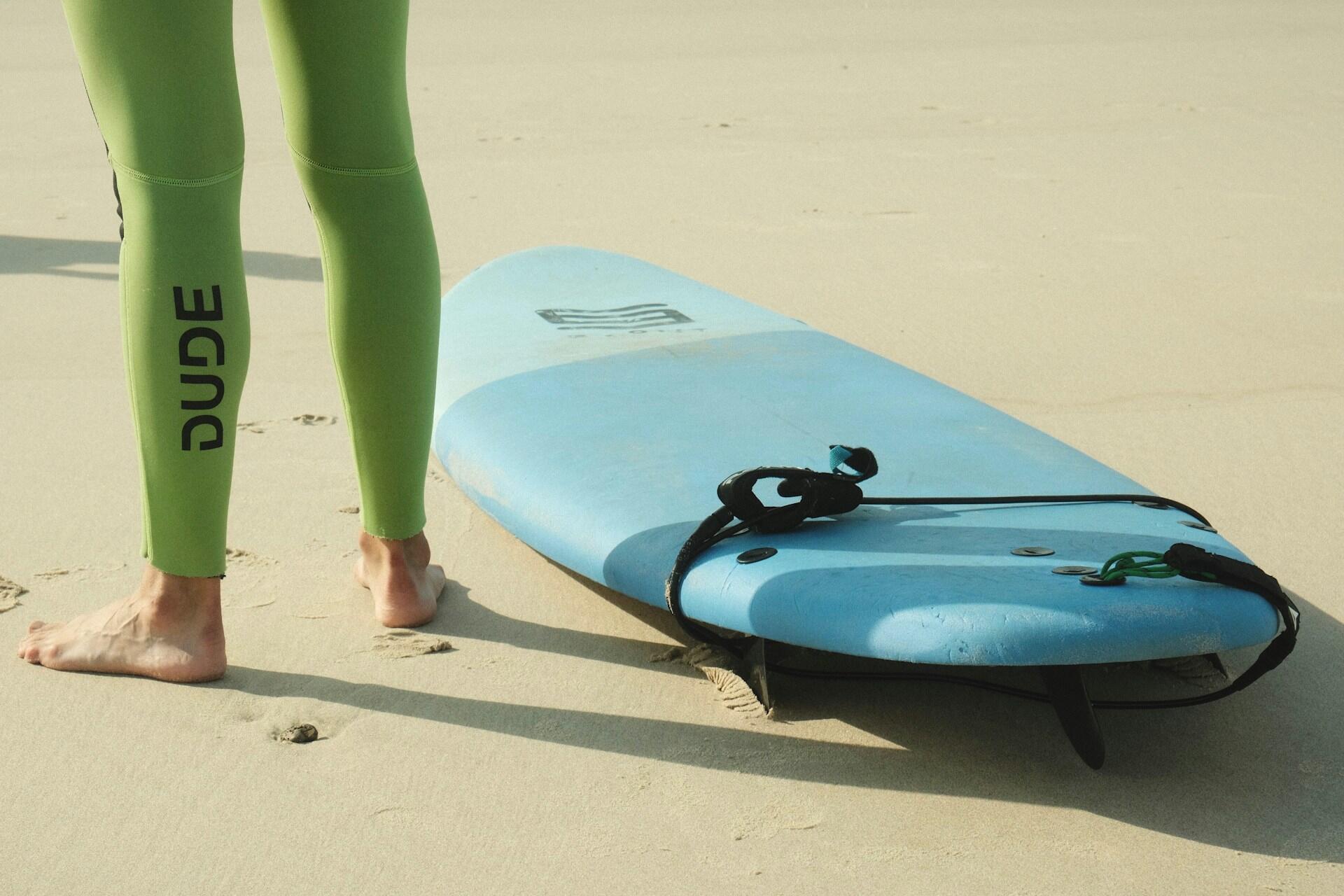 A surfboard with leash next to a person wearing a green wetsuit