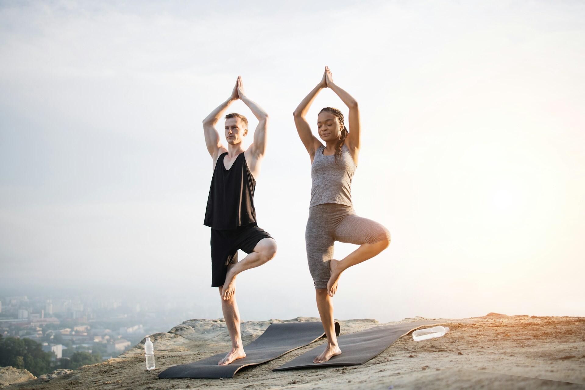 Two people on a beach holding a yoga pose.