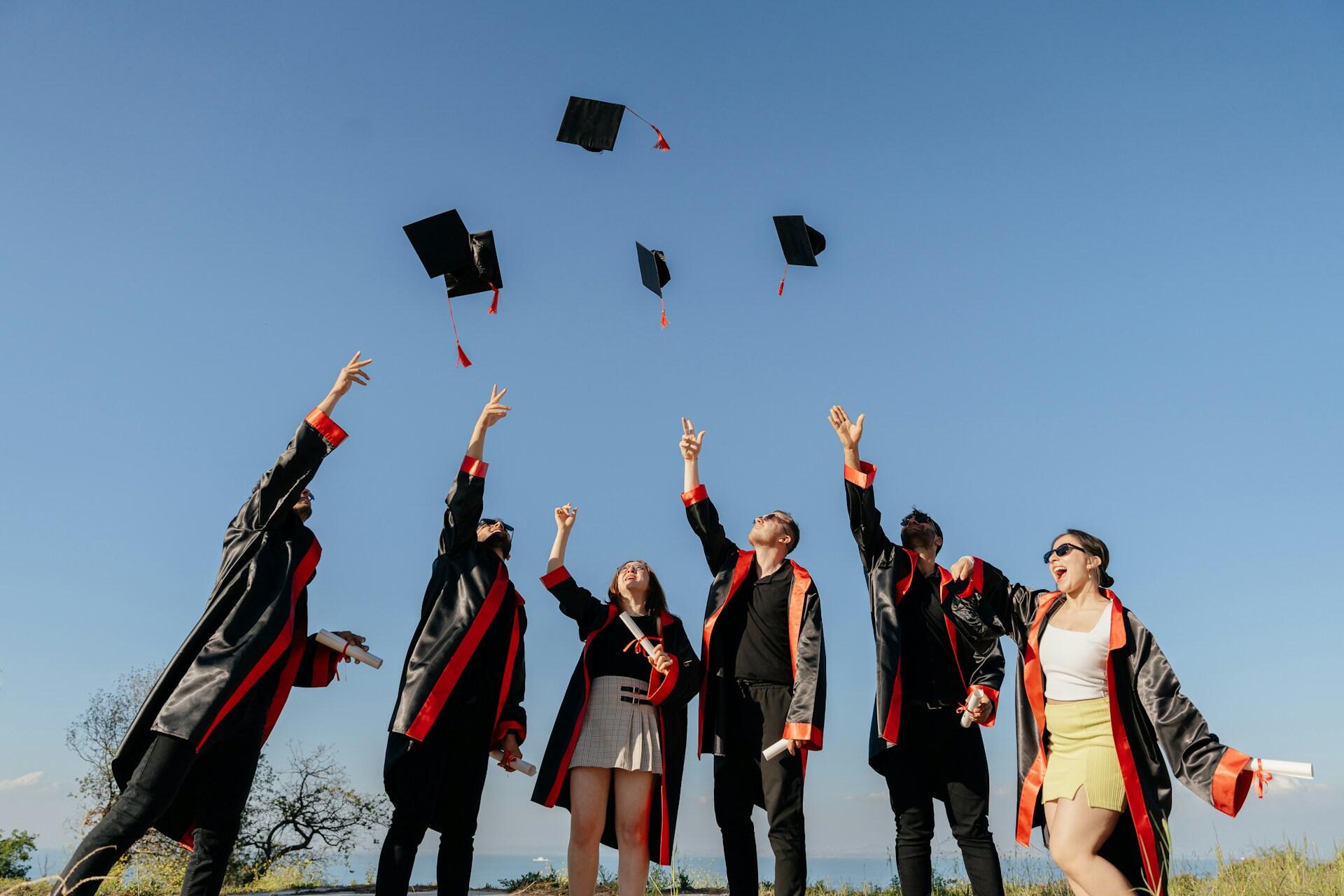 A group of graduates in caps and gowns joyfully toss their graduation caps into the sky.