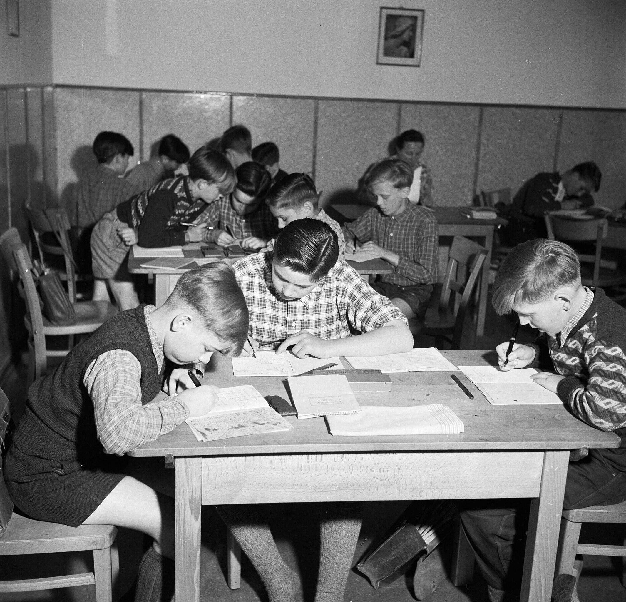 black and white photo of young Dutch schoolchildren completing homework together in 1955