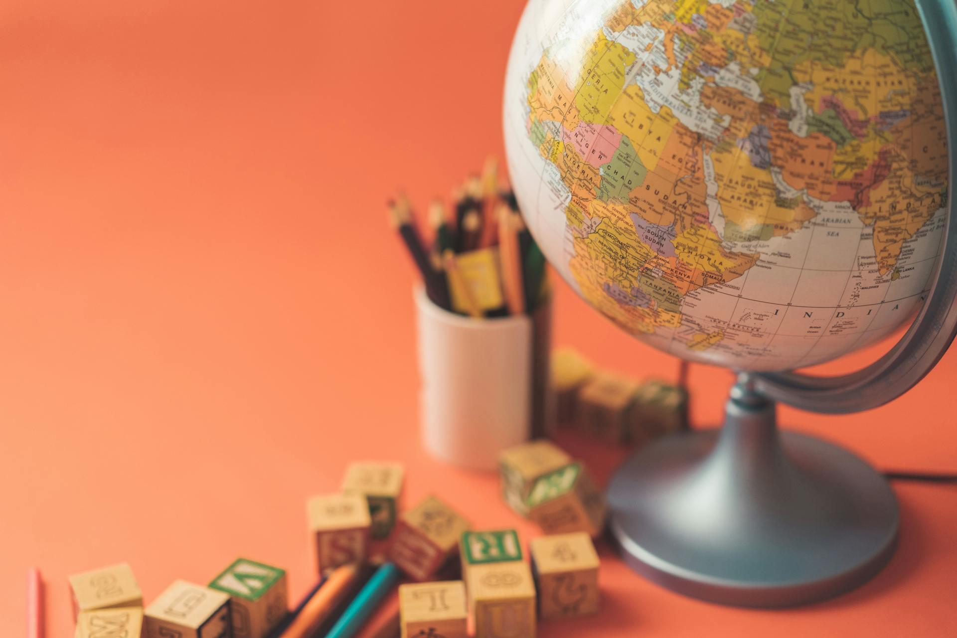 a globe, a cup of pencils, and some wooden alphabet blocks on an orange background