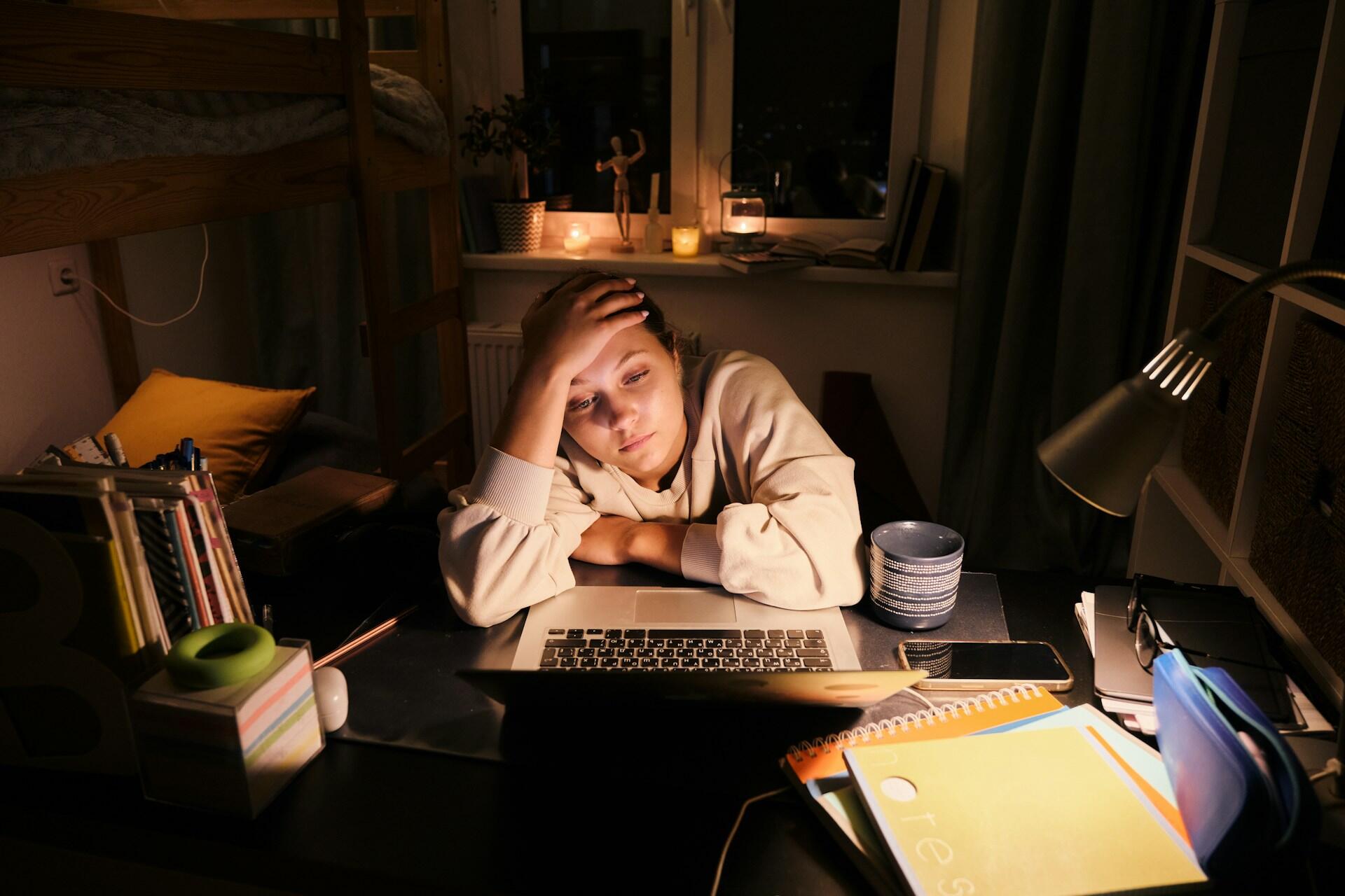 tired student looking fatigued, staring at a computer screen at night