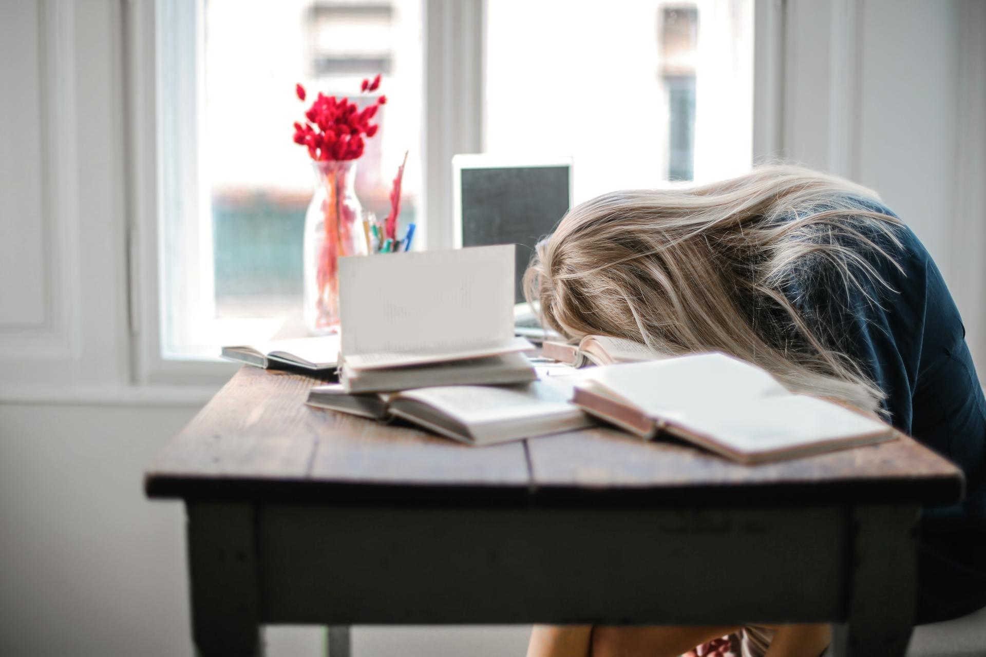 a student laying face-down in a textbook from stress and exhaustion while doing homework
