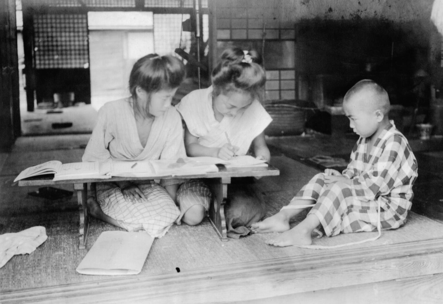 black and white photo of two women and a child completing homework in Japan