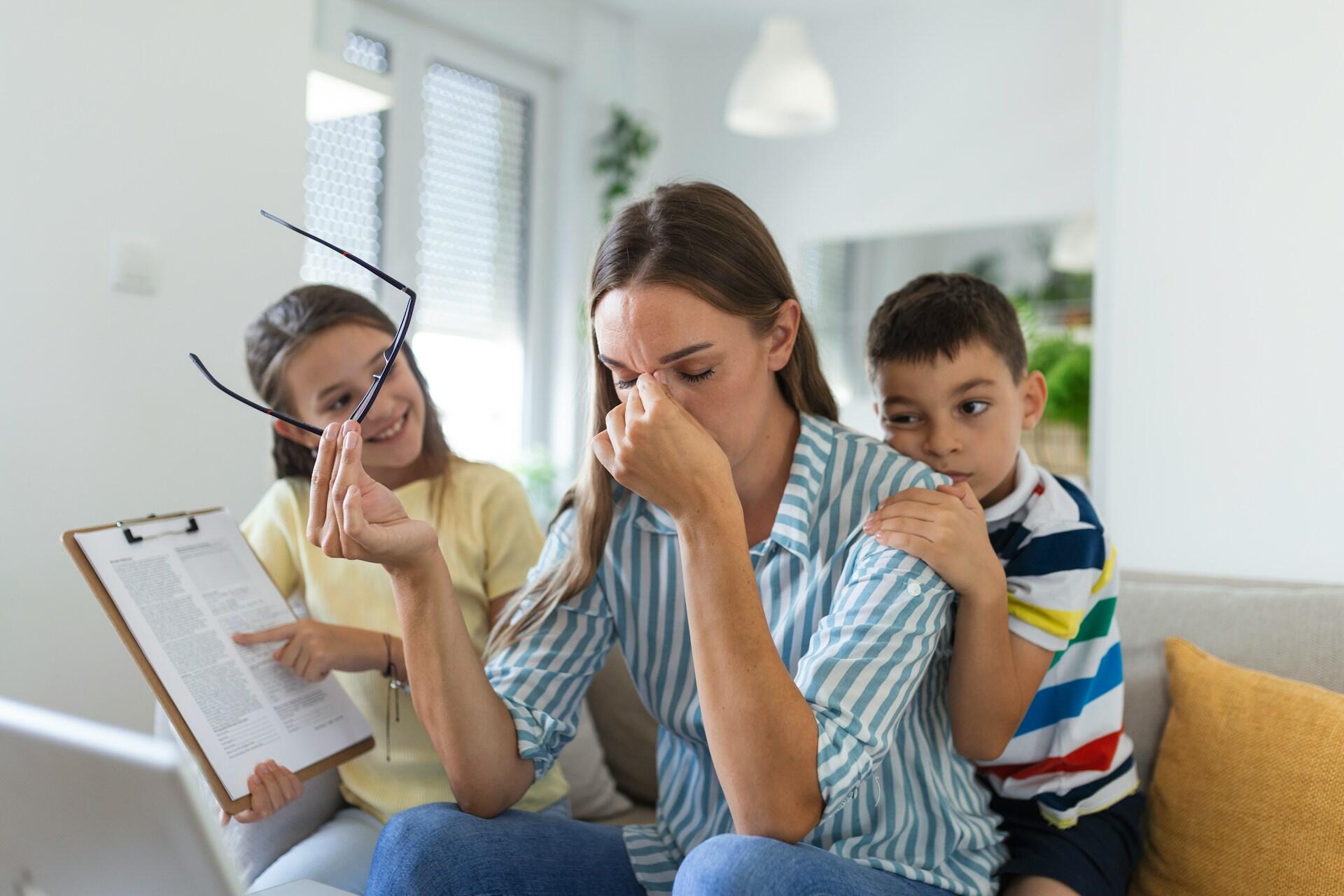 a child showing instructions to her mother, who is stressed about the information and also has a younger child on her back