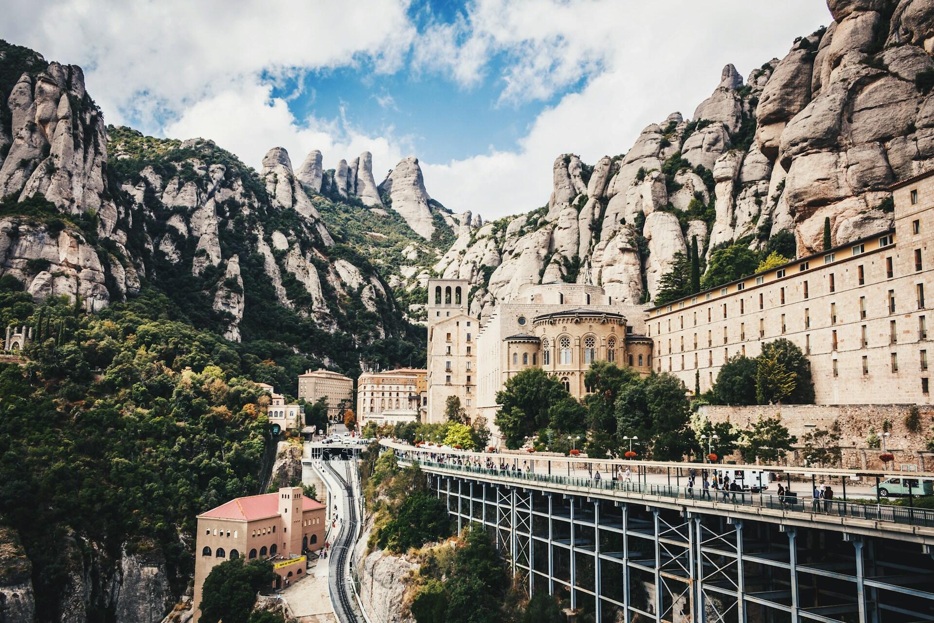 View of Montserrat in Spain, featuring rock formations, a monastery, and visitors on a walkway.