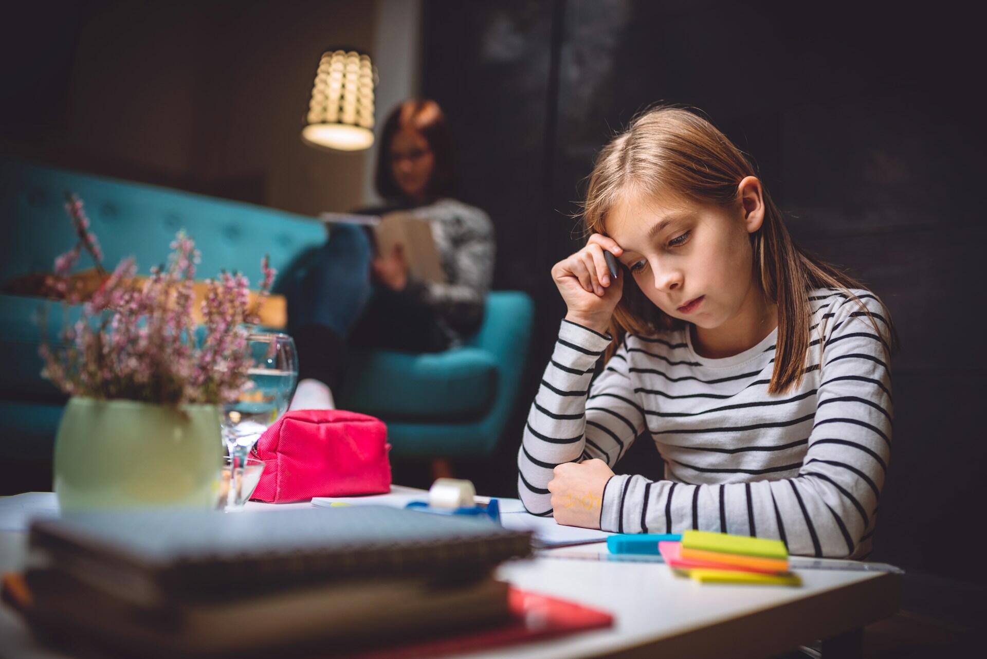 a young student looking stressed sitting at a table at night trying to finish homework