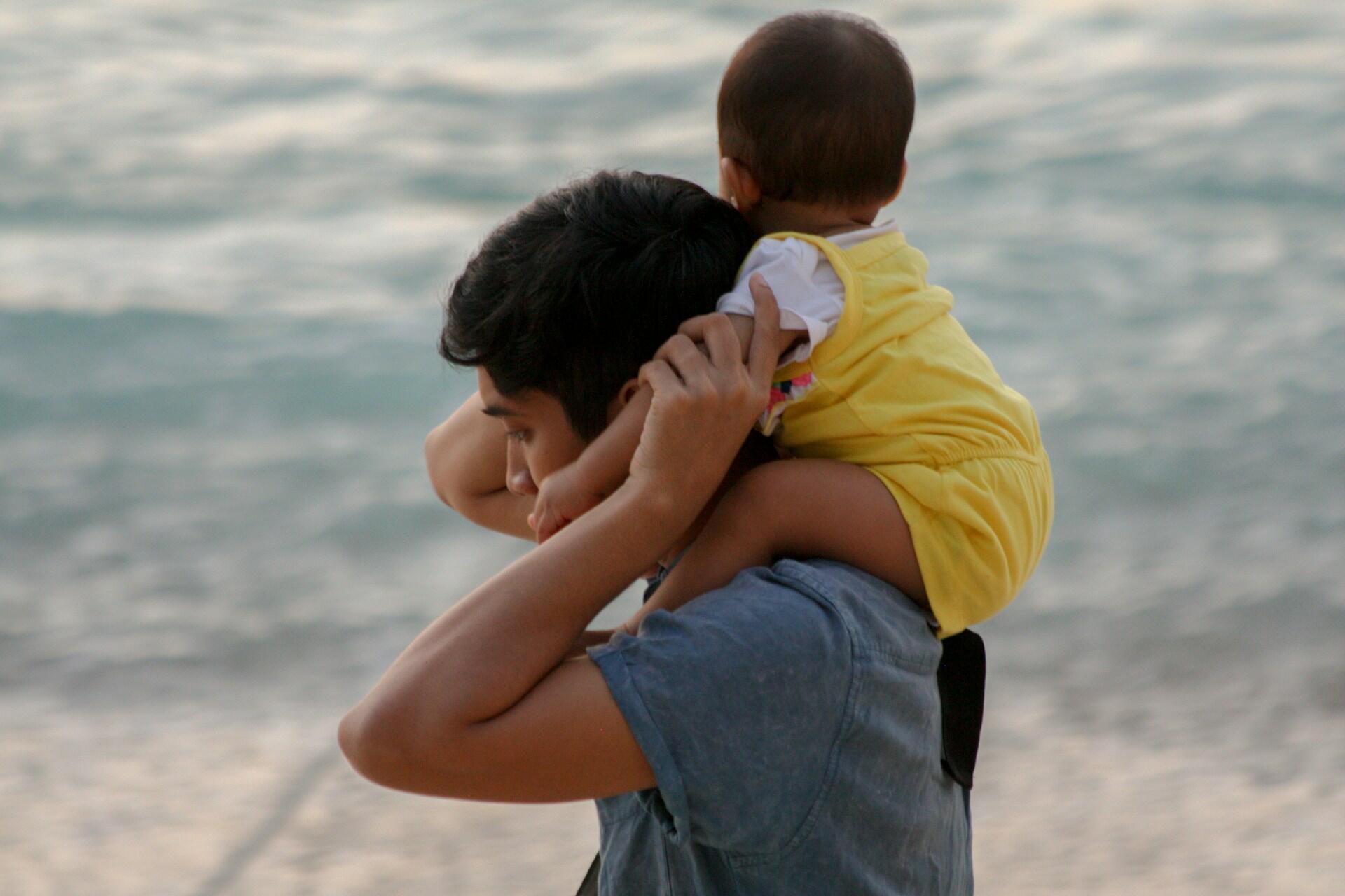 A person carries a child on their shoulders at the beach.