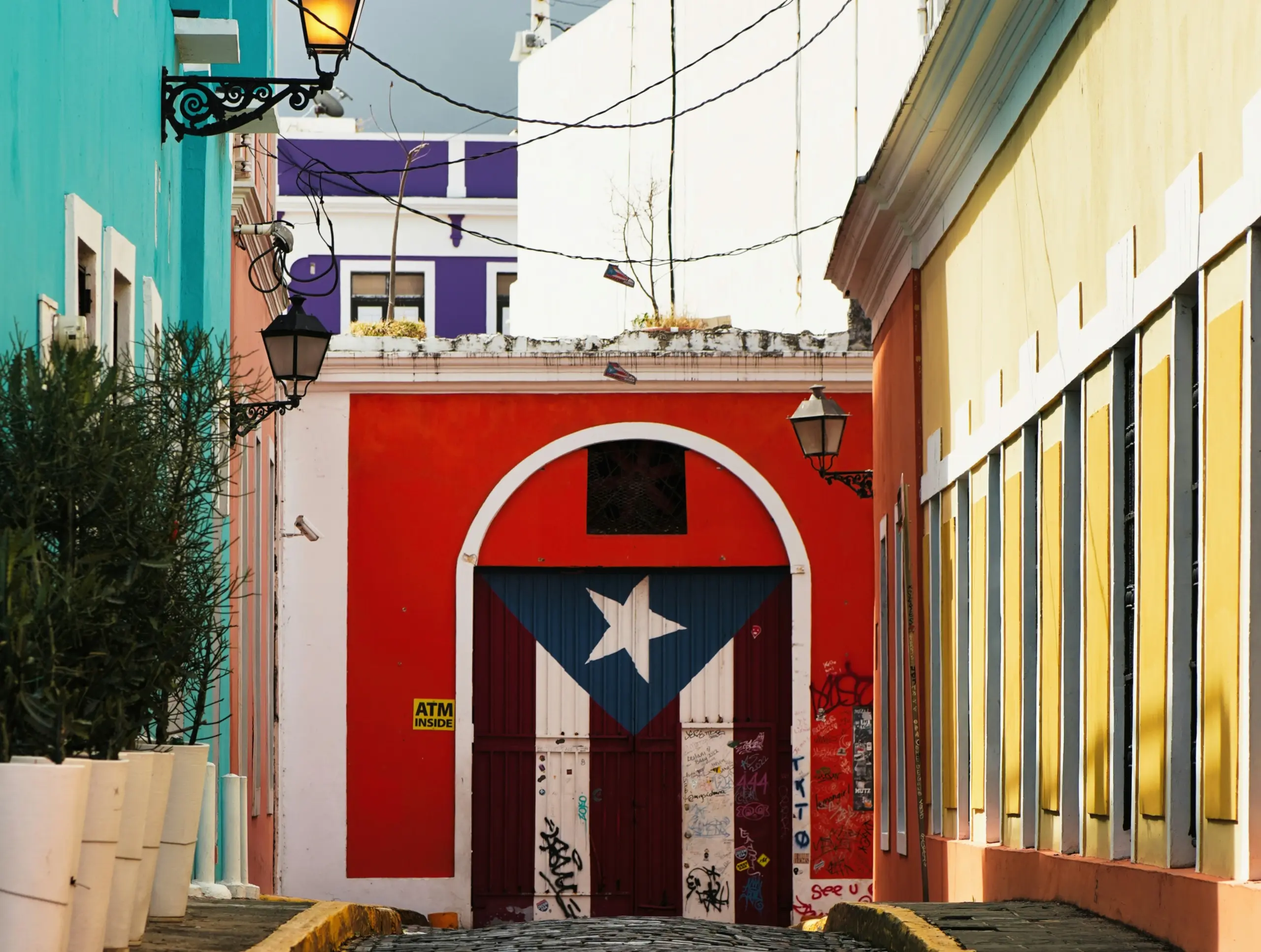 A vibrant alleyway with colorful buildings, featuring a red door adorned with the Puerto Rican flag and bold yellow window shutters.