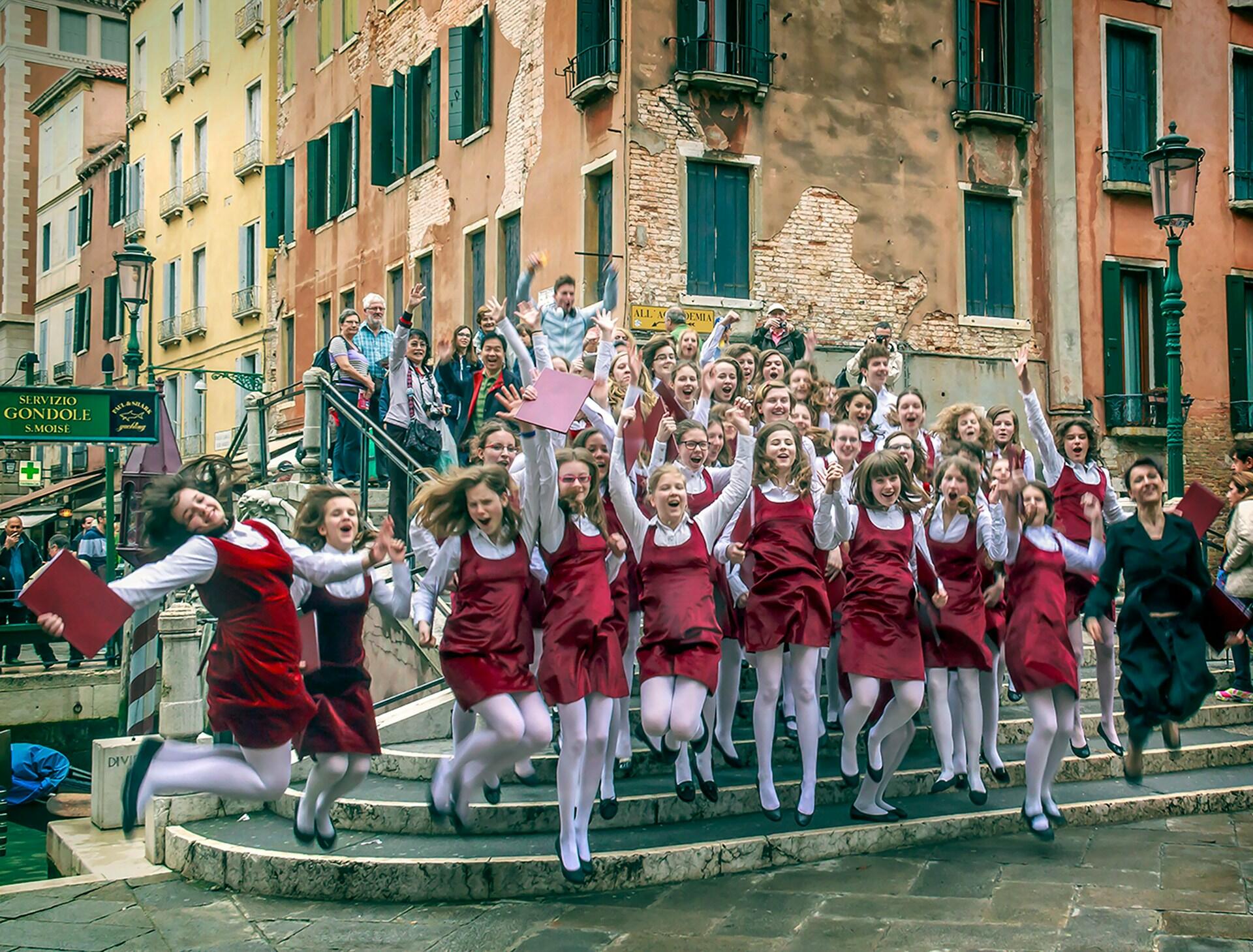 A group of girls wearing red and white pose excitedly in front of a stone building.