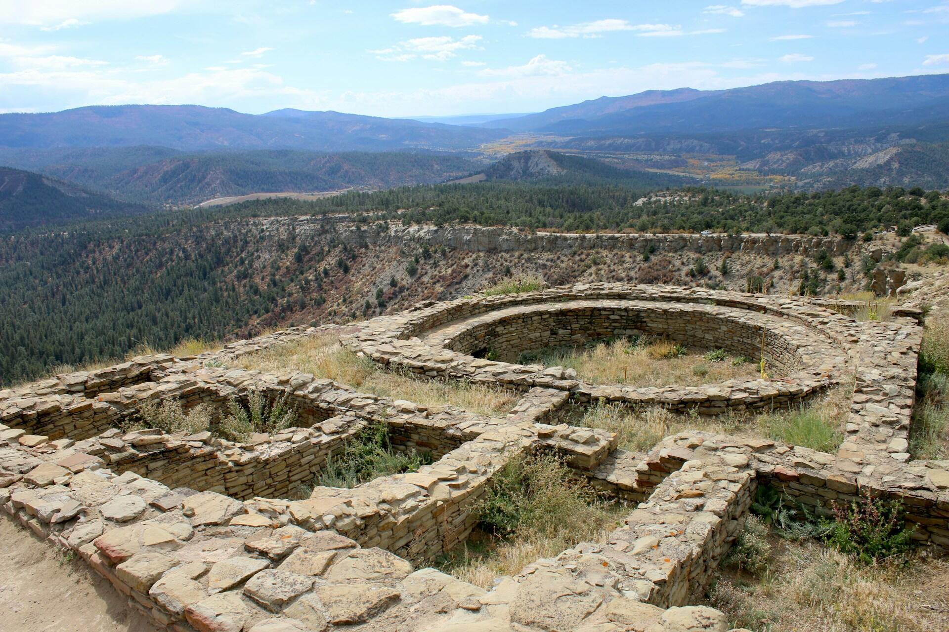 Ancient ruins with stones laid in a circle and a path leading to them on a hilltop on a sunny day.