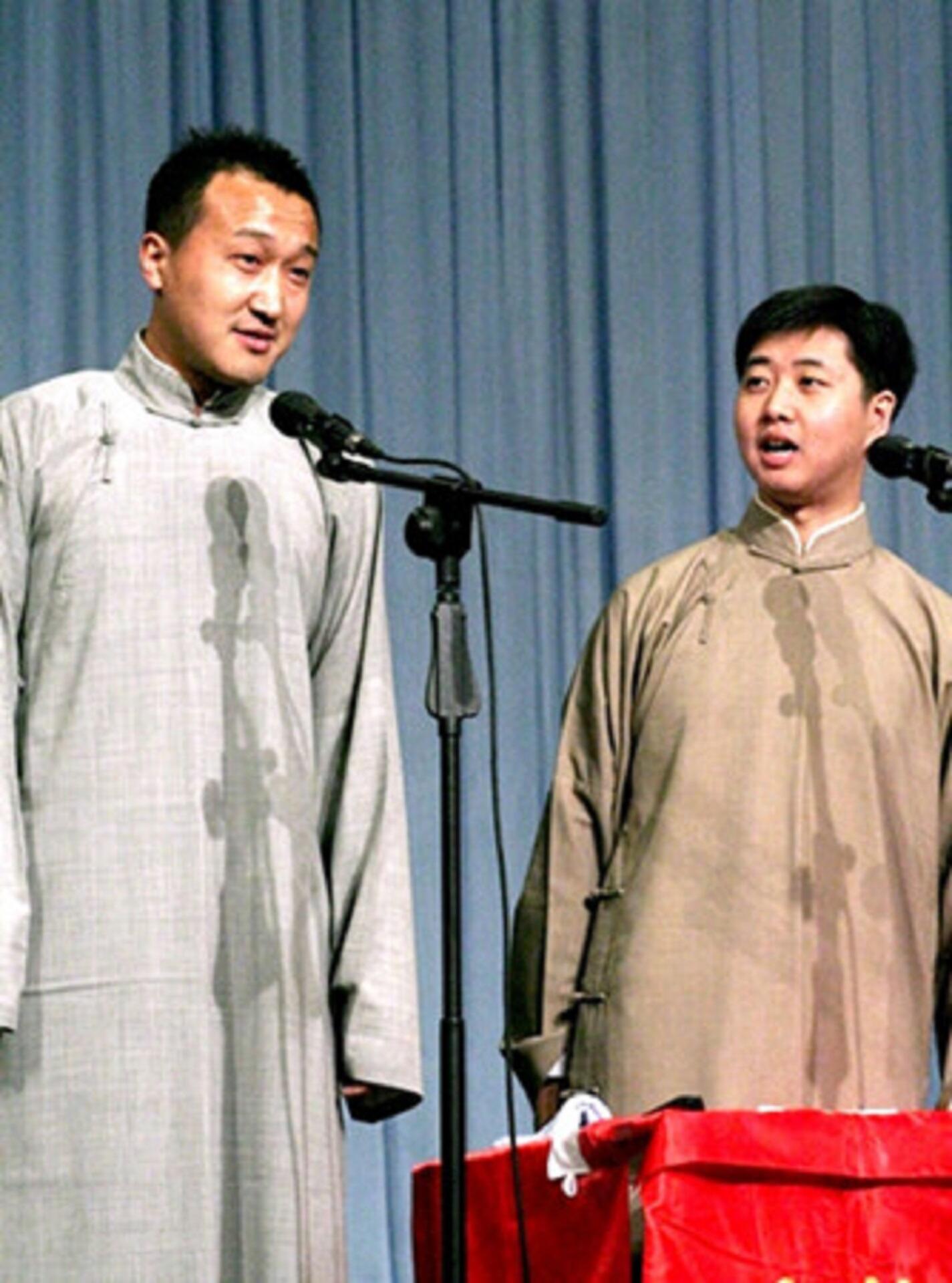 Two men wearing traditional Chinese clothing in front of microphones.