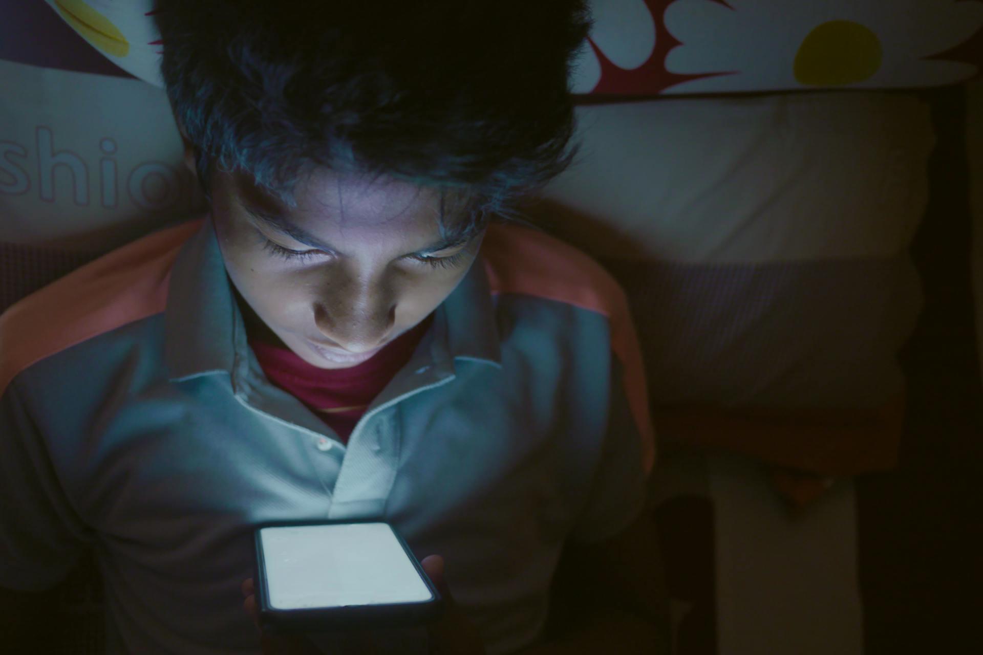young teen using a phone in the dark, looking distressed