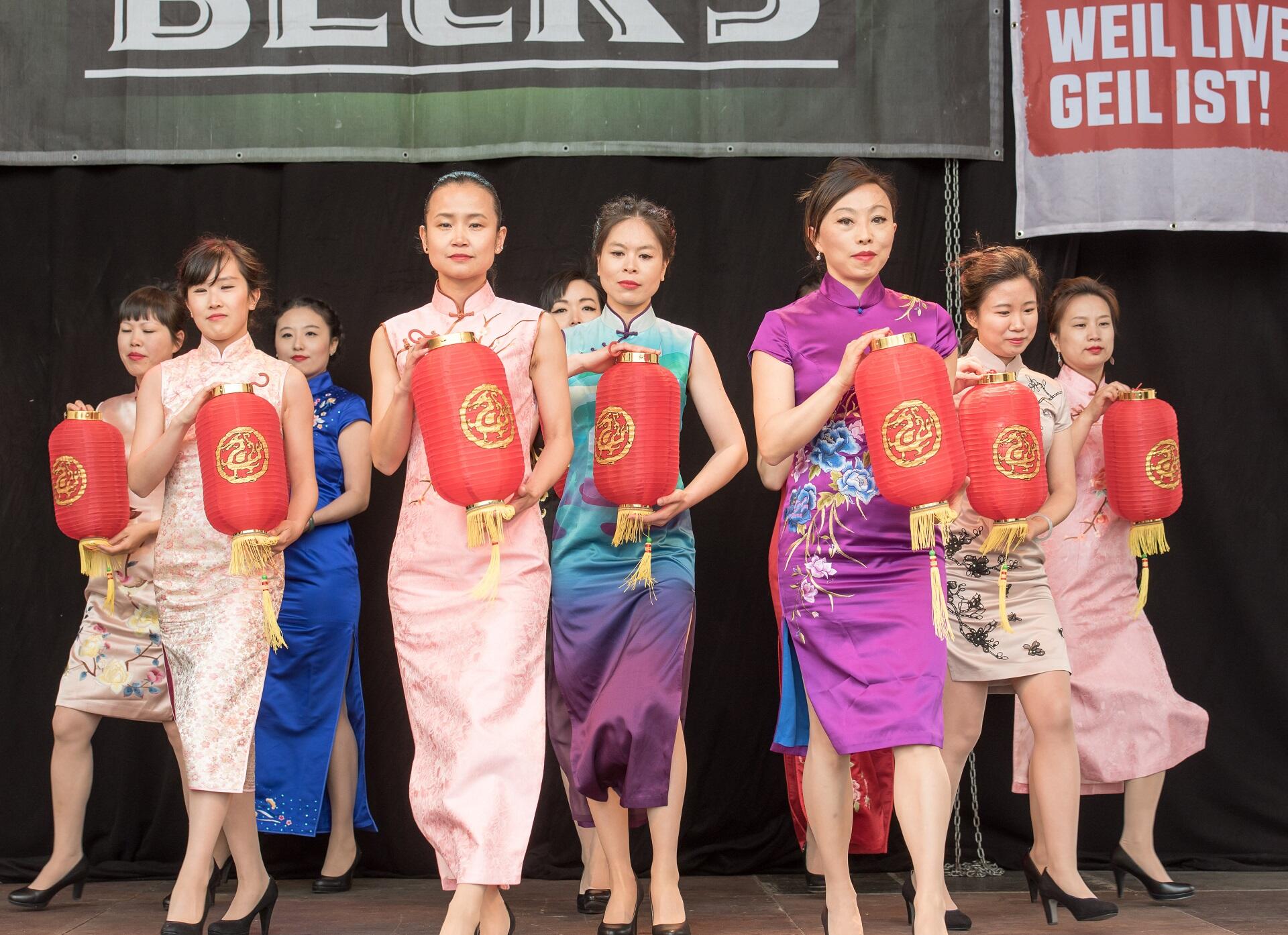Women wearing qipao on stage holding Chinese lanterns.