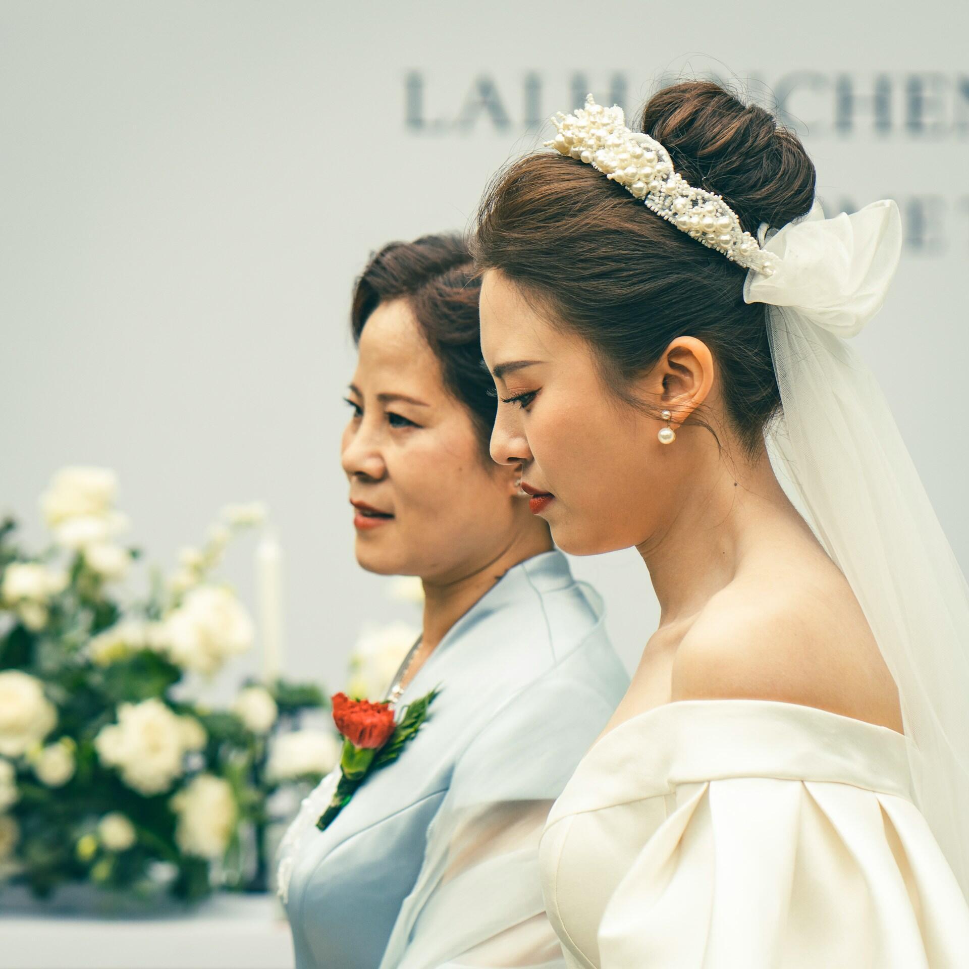 Two women, one wearing white clothing with an upswept hairstyle. 