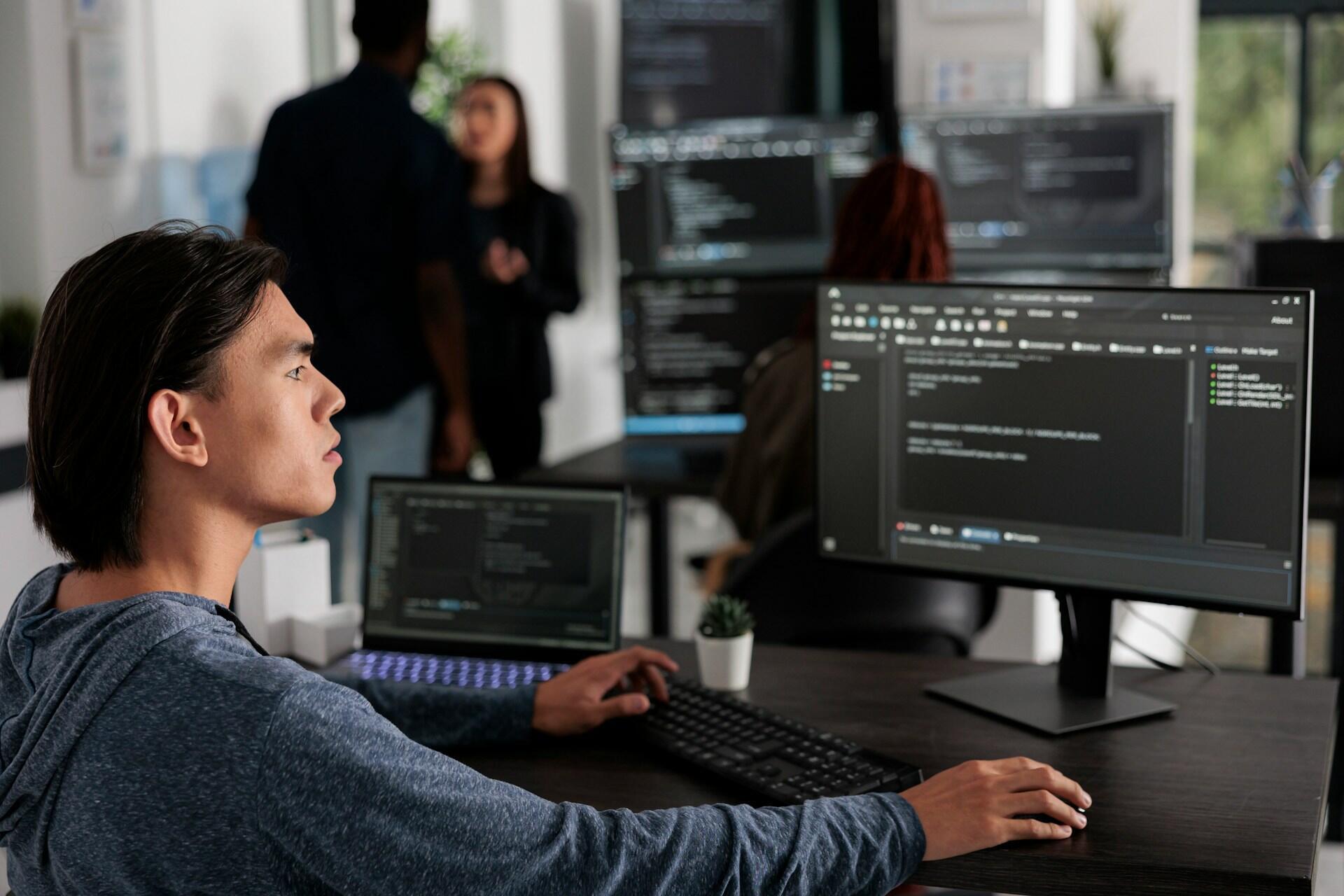 A man working on a desk on a computer with multiple screens.