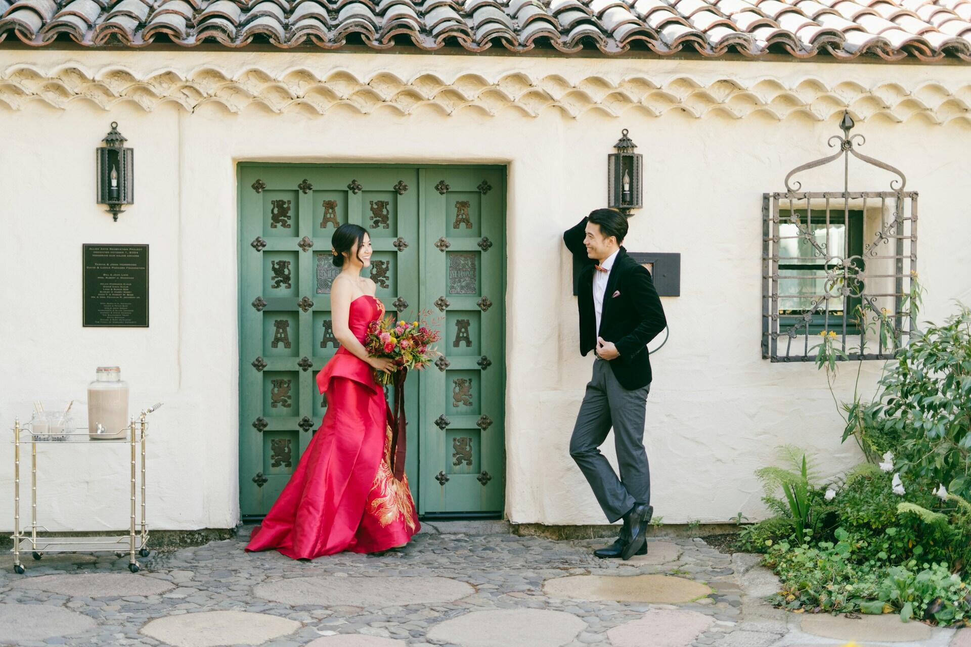 A woman in a red dress stands in front of a green door with a man in a suit.