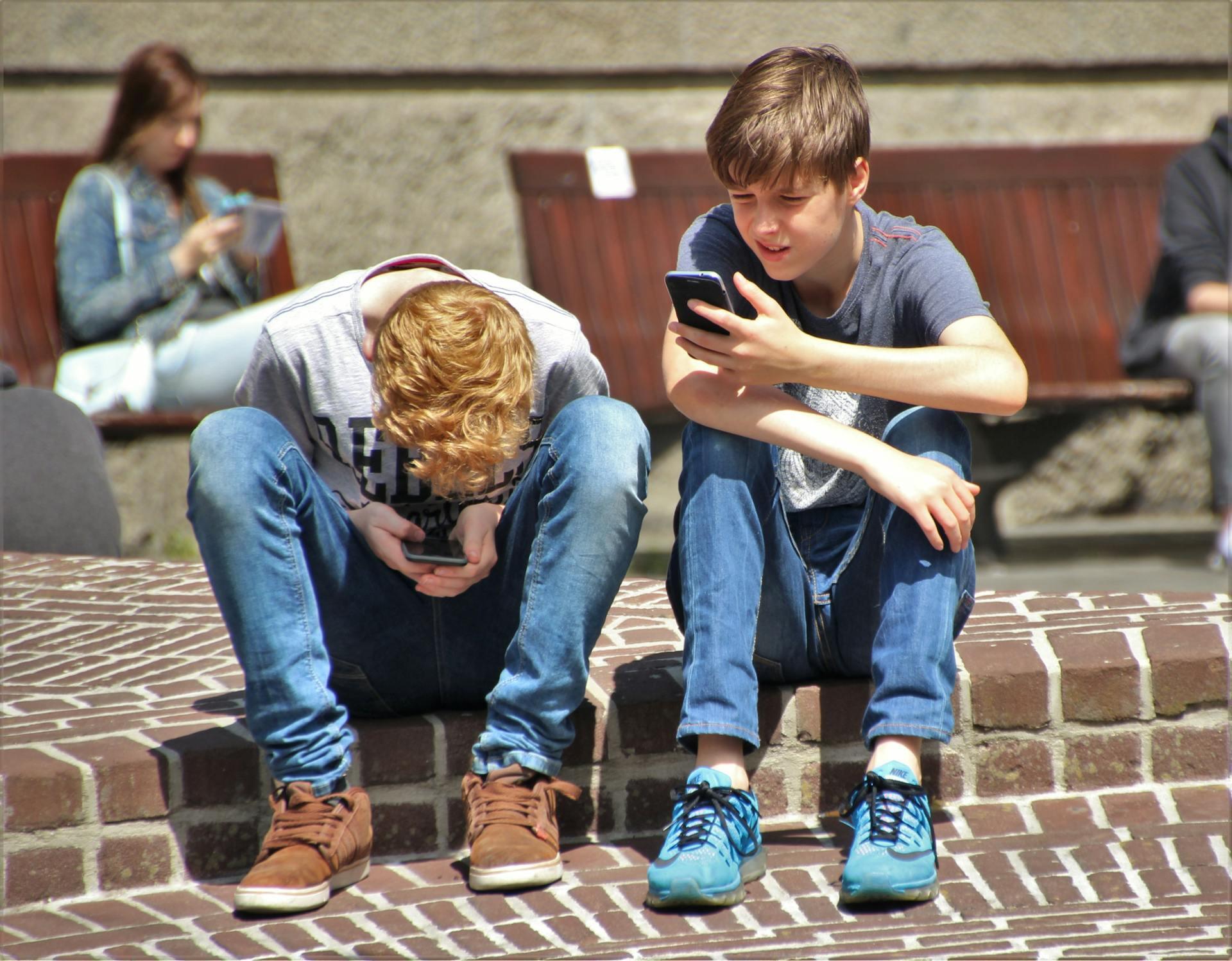 two teen boys using smartphones outside