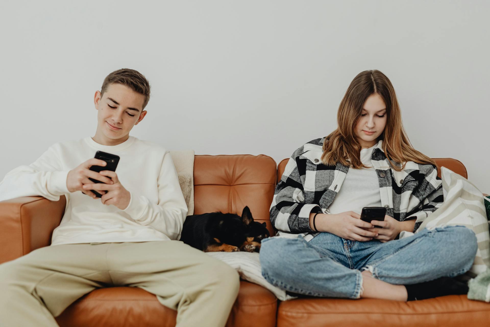 two teens sitting on a couch using their respective phones