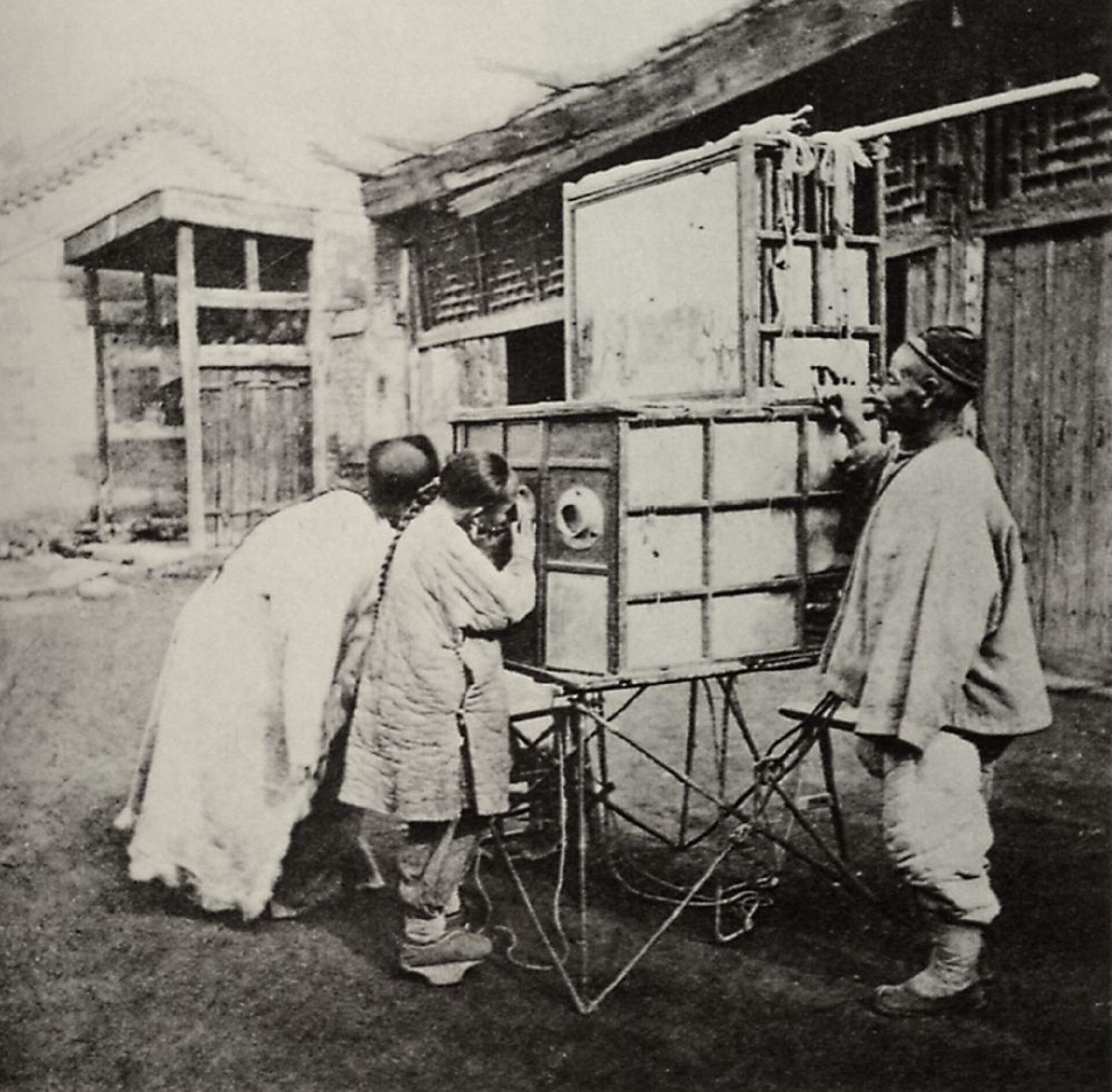 Three people in Chinese dress peep into an enclosed wagon. 