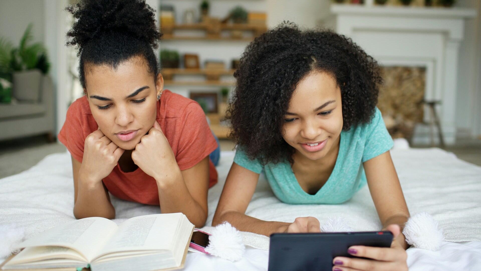 two young students, one reading from a book and one using a tablet