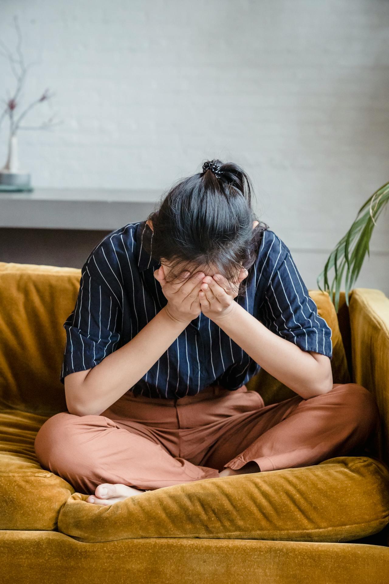 woman sitting on a couch, crying, with her face in her hands