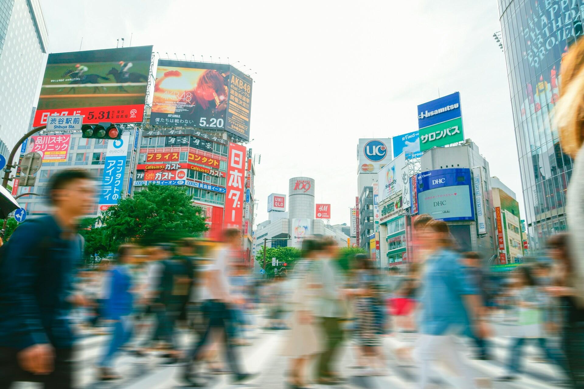 A bustling Shibuya intersection with colourful billboards and a crowd of people.