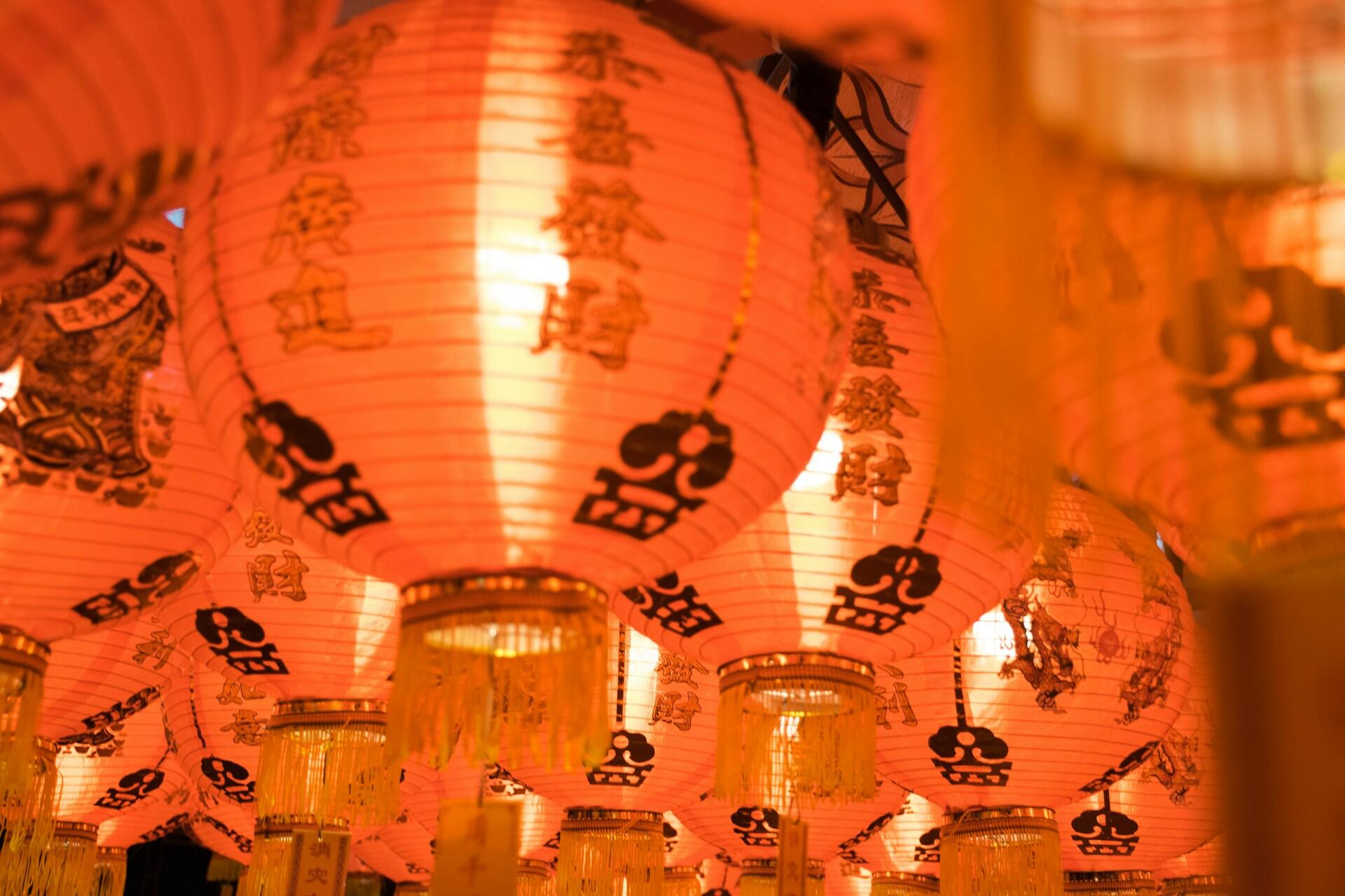 A vibrant display of red lanterns, adorned with intricate black designs, illuminates a festive setting.