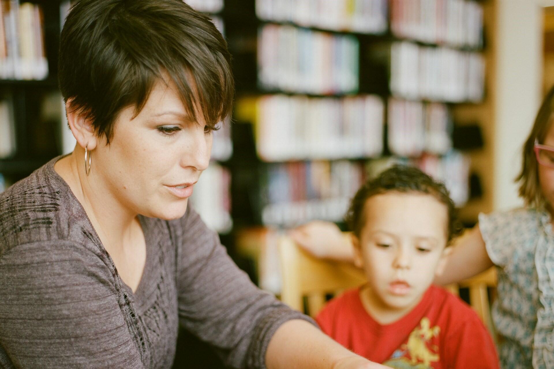 Adult helping a young child with an activity at a table in a library.
