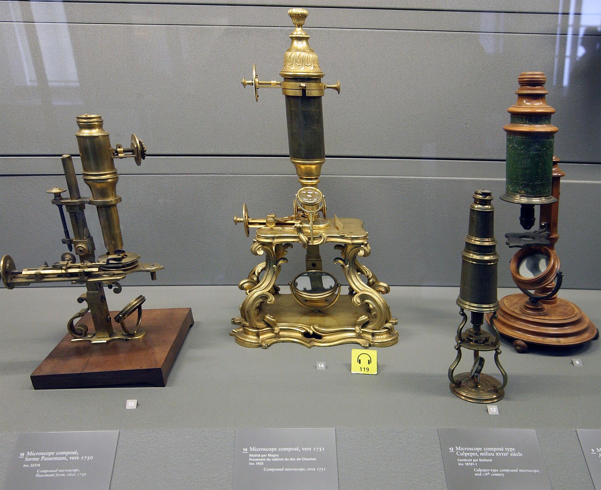 Three antique microscopes in a museum display case.