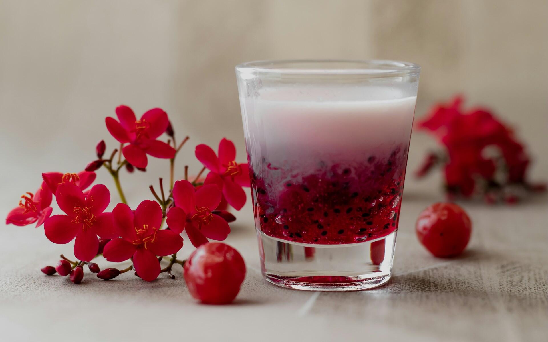 A glass containing red and white liquids, surrounded by red flowers. 
