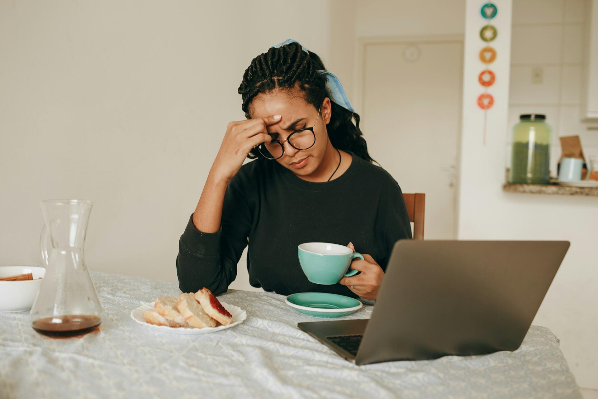 Person sitting at a table with a laptop and notebook while holding a cup of tea.