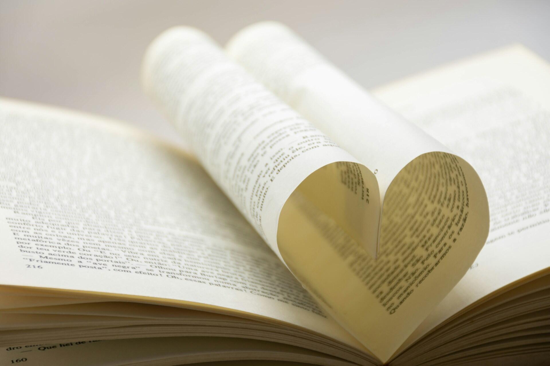 A close-up of an open book with a page folded into the shape of a heart, resting on another open page filled with text.