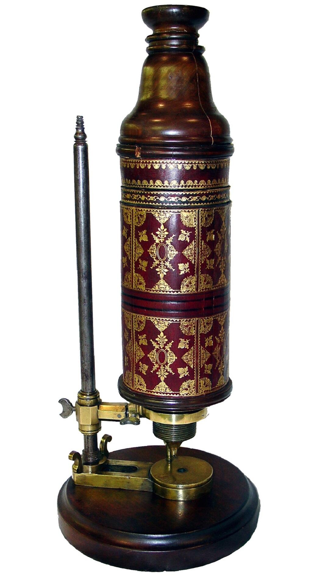 An antique microscope with gold inlaid red leather wrapping the body.