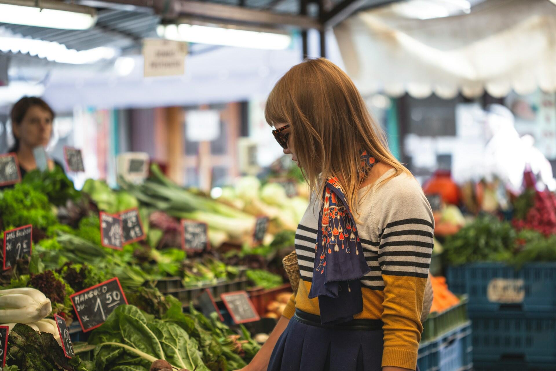 Person browsing fresh vegetables at an indoor market stall.