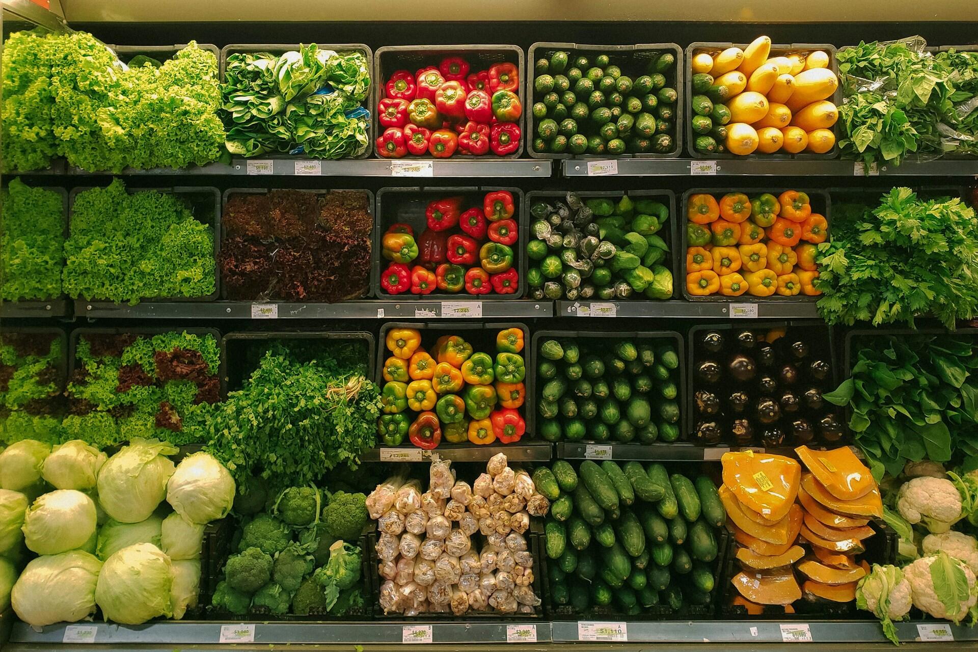 Fresh vegetables arranged in rows on a supermarket produce shelf.