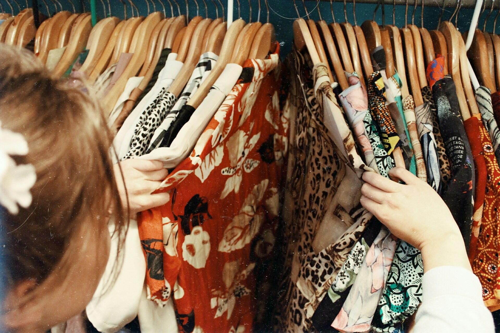 Person browsing patterned clothing on wooden hangers in a wardrobe or shop rail.