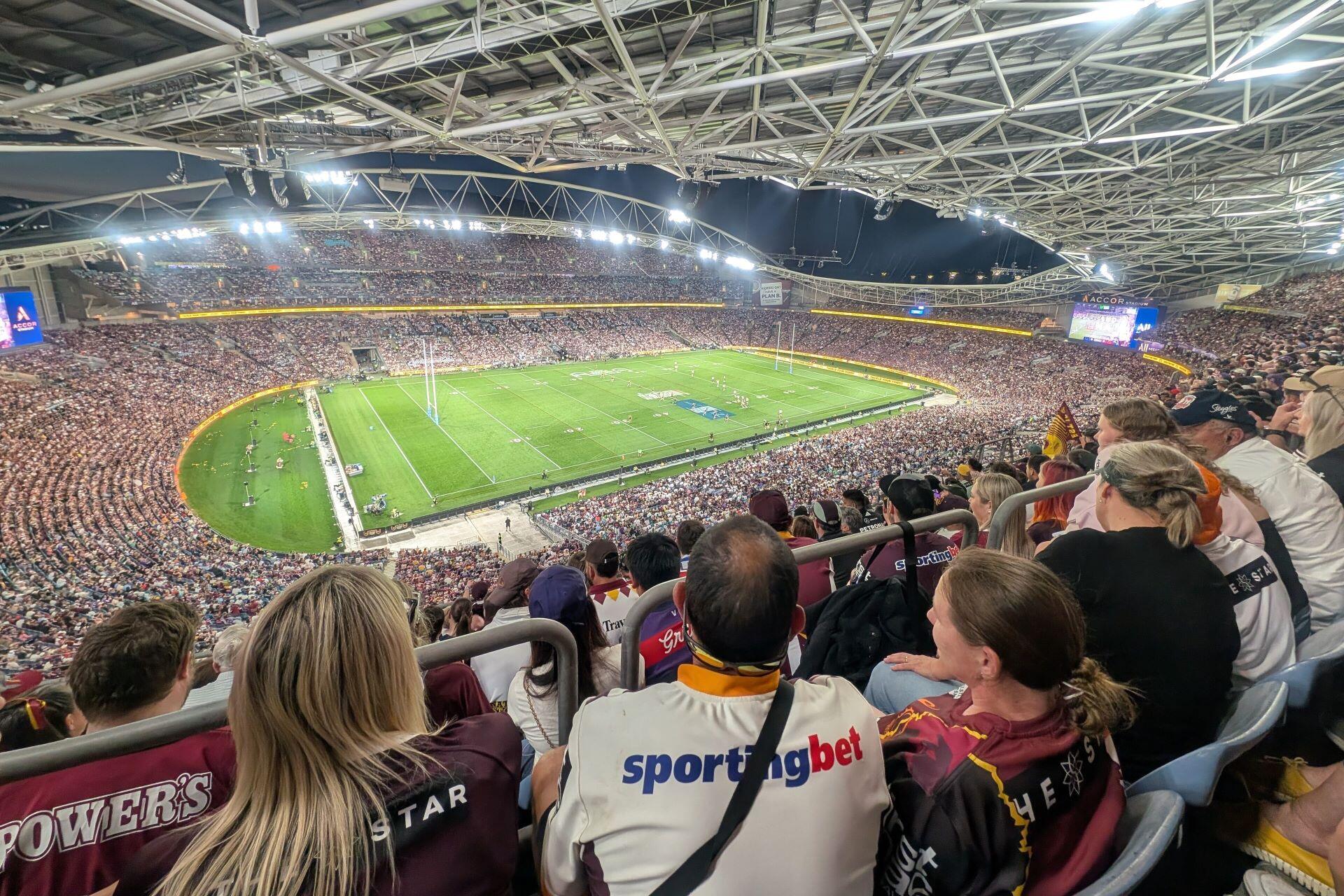 Fans watching an NRL match inside a packed modern rugby league stadium