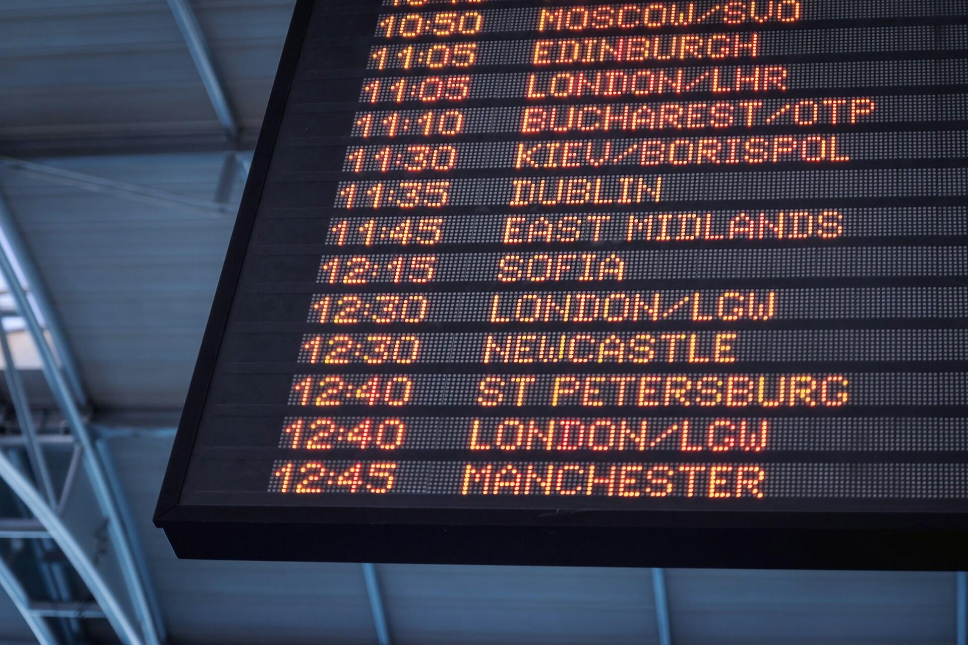 A digital airport schedule board showing times and city names in orange lights.